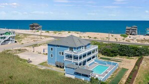 A large, multi-story blue building with a pool, located near a beach with a clear view of the ocean. - Premier Semi-Oceanfront w/ Pool, Hot Tub, Elevator, Theater, Bocce/Putting Court (Rodanthe)