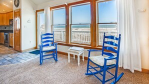 A room with a view of the beach, two blue rocking chairs, a small table, and wooden cabinets. - Premier Semi-Oceanfront w/ Pool, Hot Tub, Elevator, Theater, Bocce/Putting Court (Rodanthe)
