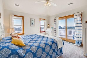 Une chambre avec un grand lit, un ventilateur de plafond et un balcon avec des rideaux.