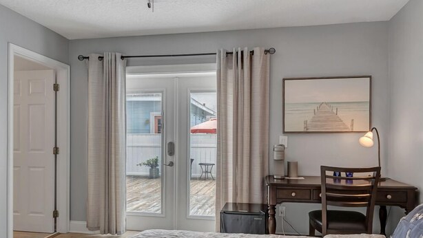 A bedroom with a bed, a desk, a chair, and a view of a patio with a table and chairs.