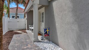 A covered patio area with a white fence, palm trees, and a flag on the wall.