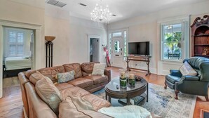 A spacious living room with a large brown leather sofa, a coffee table, and a chandelier. - Sunny Side Cottage walkable to downtown w/ garden (St Augustine)