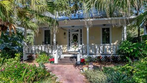 A yellow house with a porch, surrounded by lush greenery and plants. - Sunny Side Cottage walkable to downtown w/ garden (St Augustine)