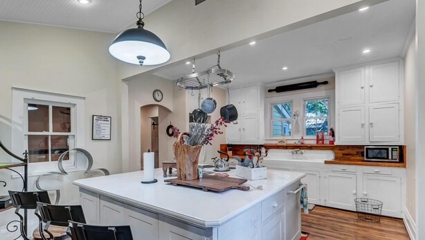 A modern kitchen with white cabinetry, a central island, and a hanging pot rack. - Sunny Side Cottage walkable to downtown w/ garden (St Augustine)