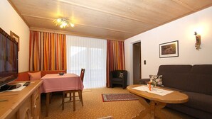 Sala de estar com teto de madeira, mesa de jantar com toalha de mesa rosa, sofá marrom e televisão sobre um armário de madeira.