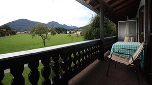 Uma varanda com uma cama, vista para um campo verde e montanhas ao longe.