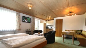 Ein Zimmer mit zwei Betten, Holzbalkendecke, Fernseher, einem kleinen Tisch mit einer Schale, einem Sessel und einer Couch.