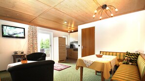 Ein gemütliches Zimmer mit einer Couch, einem Tisch, einem Fernseher und einer Küche im Hintergrund.