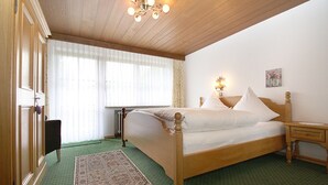 Ein ordentlich eingerichtetes Schlafzimmer mit einem Holzbett, einem grünen Teppich und einem großen Fenster mit leichtem Vorhang.