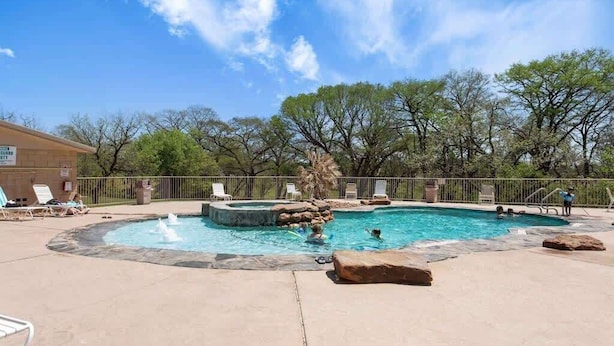 A swimming pool with a hot tub, surrounded by lounge chairs and a fence. - Relax by the River | Shared Pool | Labor Day Ready (New Braunfels)