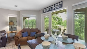 A dining area with a table set for four, surrounded by a balcony with a view of greenery. - Relax by the River | Shared Pool | Labor Day Ready (New Braunfels)