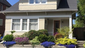 Una casa de dos pisos con un porche delantero, una chimenea y una variedad de flores coloridas en el jardín.