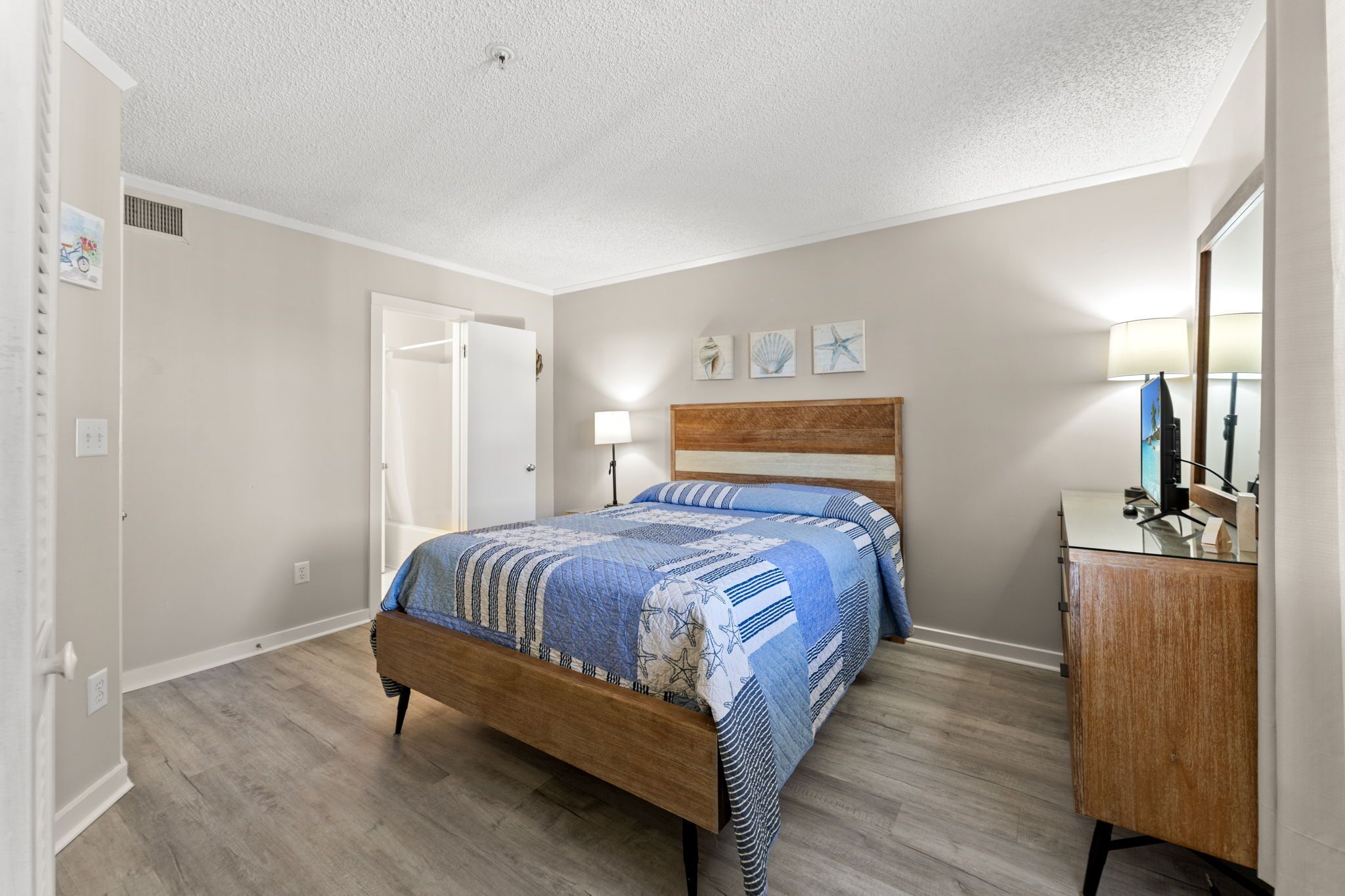 A bedroom with a wooden bed, a bedside table, a lamp, and a dresser.