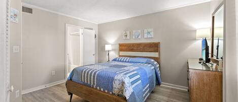 A bedroom with a wooden bed, a bedside table, a lamp, and a dresser.