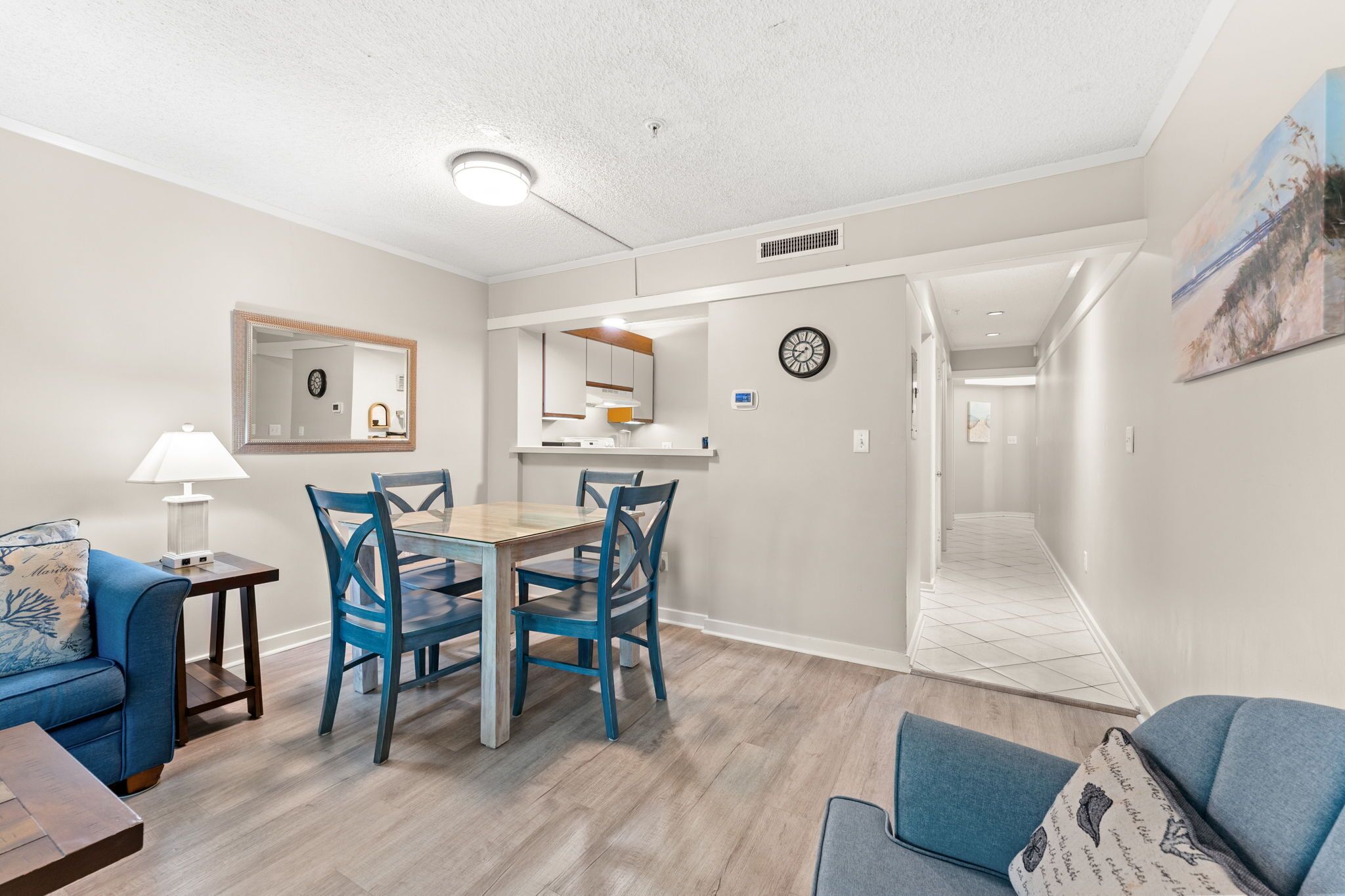 A modern living room with a dining area, a kitchen, and a hallway leading to another room.