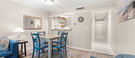 A modern living room with a dining area, a kitchen, and a hallway leading to another room.