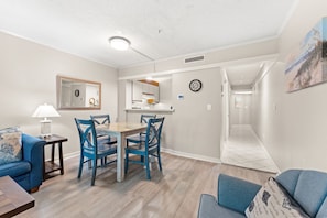 Een moderne woonkamer met een eethoek, een keuken en een gang die naar een andere kamer leidt.