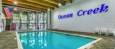 An indoor swimming pool with a wooden ceiling and a large American flag. The words "Ocean Creek" are visible on the wall.