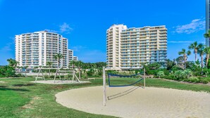 Un complexe hôtelier comprenant plusieurs immeubles de grande hauteur, une plage de sable avec un filet de volley-ball et des espaces verts environnants.