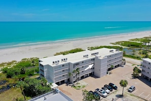 Ein mehrstöckiges Hotel mit flachem Dach, Parkplatz und Blick auf Strand und Meer.