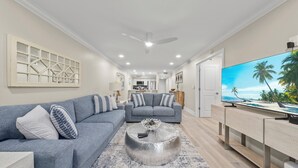 A modern living room with a grey sofa set, a coffee table, and a flat-screen TV displaying a beach scene.