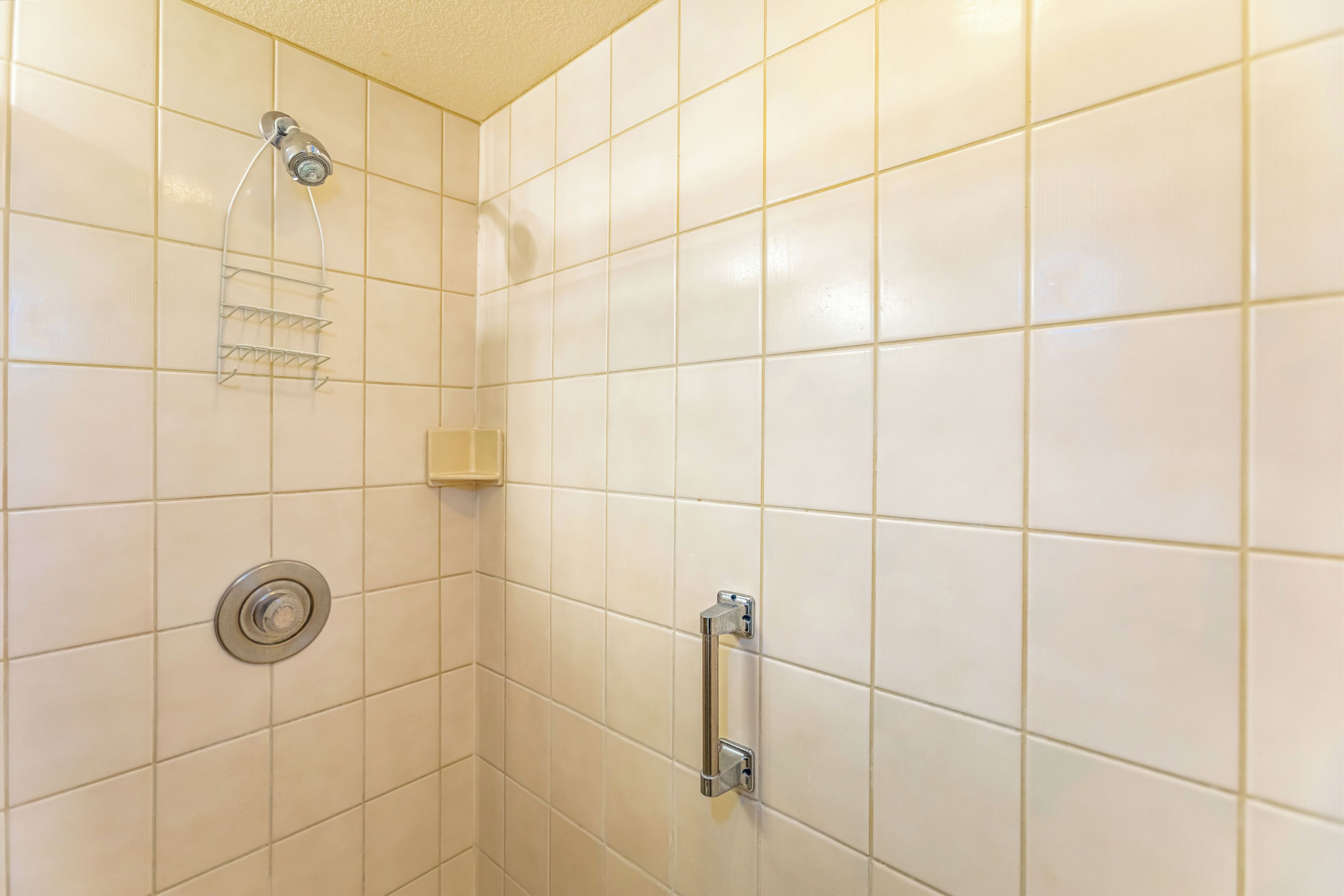 A bathroom with white tiles, a shower with a handheld showerhead, a towel rack, and a toilet with a grab bar.