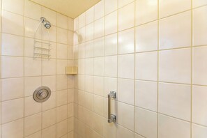 A bathroom with white tiles, a shower with a handheld showerhead, a towel rack, and a toilet with a grab bar.