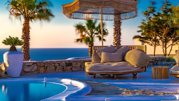A poolside area with a lounge chair, a thatched umbrella, and a view of the ocean. - Karkos Beachfront Villa  Private pool (Mykonos)