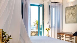 A bedroom with a large bed, a bench, a vase with flowers, and a view of the sea. - Karkos Beachfront Villa  Private pool (Mykonos)