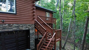 A cabin with a stone foundation, a wooden deck, and a staircase leading to a second-story balcony. - Cub Cabin on Massanutten Resort- Fully Renovated Log Cabin- Hot Tub & Fire Pit (Massanutten)