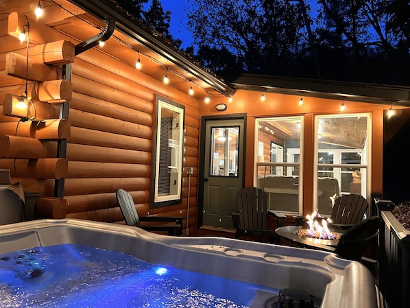 A cozy log cabin with a hot tub, string lights, and a fireplace.
