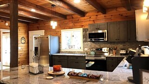 A kitchen with wooden walls, a granite countertop, a refrigerator, a microwave, and a window with a 'EAT' sign. - Cub Cabin on Massanutten Resort- Fully Renovated Log Cabin- Hot Tub & Fire Pit (Massanutten)