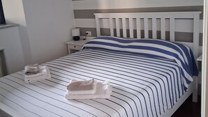 A neatly made bed with striped bedding, a white headboard, and a bedside table with a lamp and a folded towel. - Amba Alagi Apartment (citra 010025-LT-1799) (Genova)