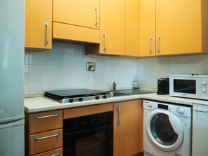Uma cozinha compacta com fogão, micro-ondas e máquina de lavar.