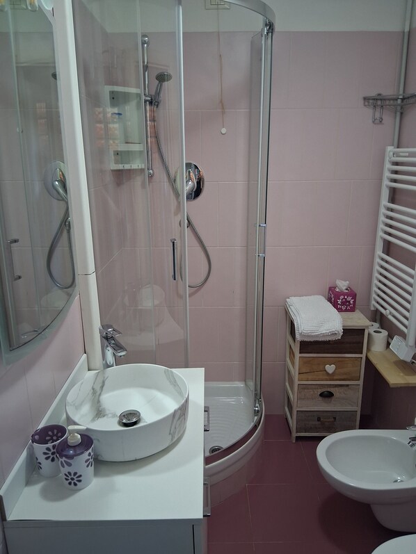 Een badkamer met een douchecabine, een wastafel met een marmeren kom, een toilet en een bidet.