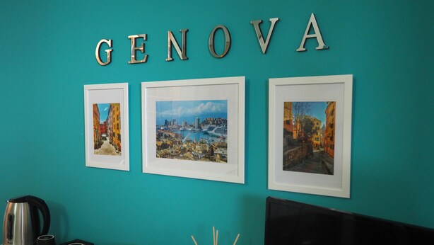 A teal wall with the word "GENOVA" and three framed cityscape photographs. - Amba Alagi Apartment (citra 010025-LT-1799) (Genova)