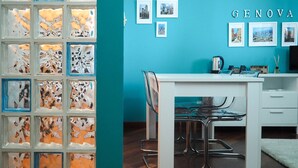 A modern room with a teal wall, a white table, and a glass partition with abstract designs. There are framed pictures on the wall and a word 'GENOVA' above them. - Amba Alagi Apartment (citra 010025-LT-1799) (Genova)
