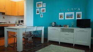 A modern kitchen with a teal accent wall, a dining area with clear chairs, and a white cabinet with a TV. - Amba Alagi Apartment (citra 010025-LT-1799) (Genova)