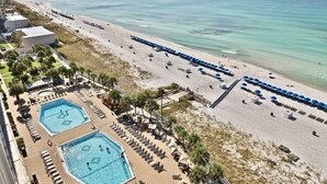 Un resort en la playa con dos piscinas, tumbonas, sombrillas y vista al océano.
