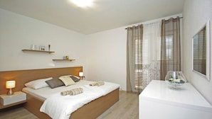 A bedroom with a wooden bed, bedside tables with lamps, a white dresser, and sheer curtains.
