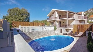 A two-story building with a swimming pool, a white fence, and a stone wall.