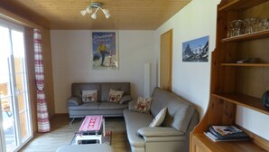 Una sala de estar con un sofá, un reposapiés, estanterías de madera y un ventilador de techo.