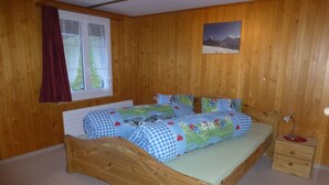 Un dormitorio con paneles de madera, una cama, una mesita de noche, una ventana con cortina y un cuadro en la pared.