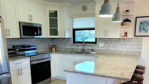 Eine moderne Küche mit weißen Schränken, Edelstahlgeräten, einer Arbeitsplatte aus Granit und einer Bar mit Barhocker.