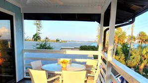 Eine überdachte Terrasse mit Tisch und Stühlen mit Blick auf ein Gewässer und Palmen.