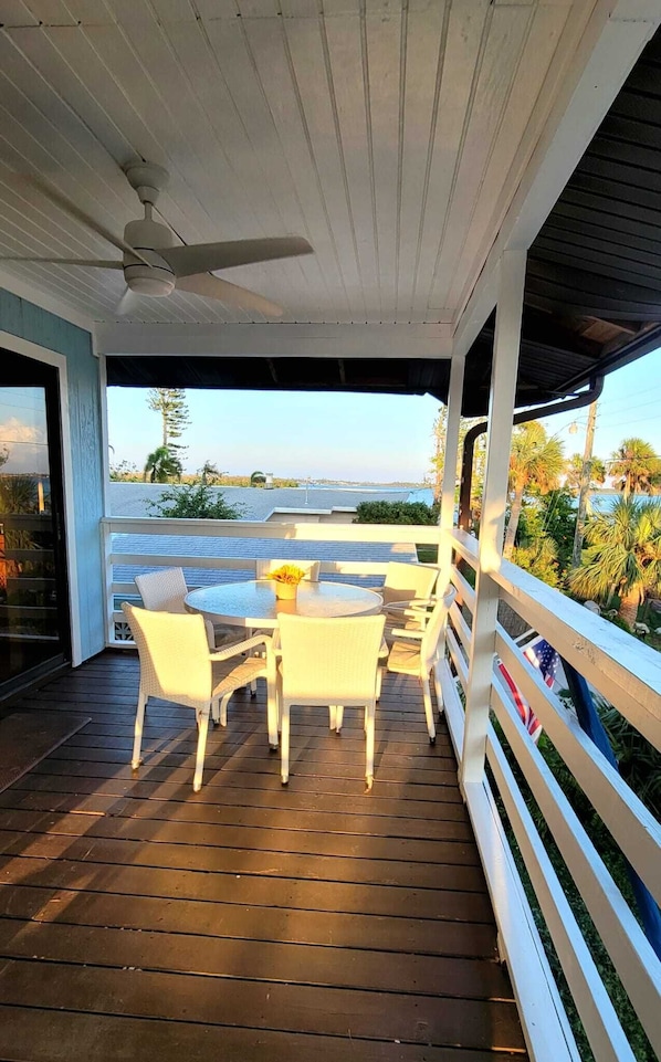 Eine überdachte Terrasse mit Tisch und Stühlen mit Blick auf ein Gewässer und Palmen.