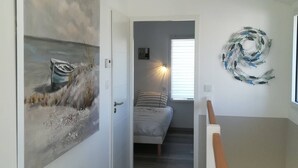 Un pasillo que conduce a un dormitorio con una cama, un cuadro de un barco en la pared, un adorno circular en la pared y una lámpara en el techo.