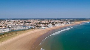 Vista aérea de una ciudad costera con una playa extensa, un puerto deportivo y una zona urbana densa.