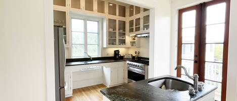A kitchen with white cabinetry, a black countertop, a stainless steel refrigerator, an oven, and a window with a view of the outside.