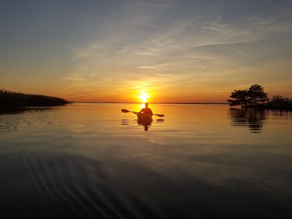 La silhouette d’un kayakiste se découpant sur le ciel d’un coucher de soleil, au-dessus d’une étendue d’eau calme.